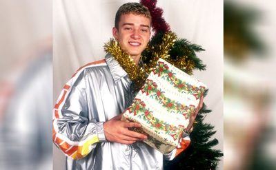 Justin Timberlake holding up a Christmas gift next to a Christmas tree