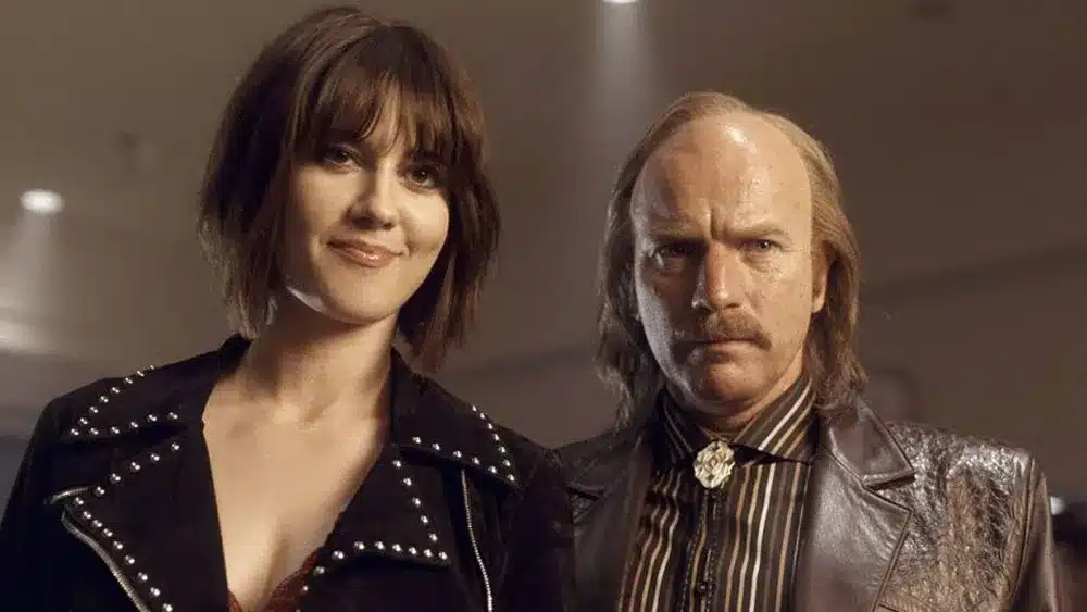 A shot from Fargo, of Mary Elizabeth Winstead with bangs and Ewan McGregor with a mustache wearing a bolo tie and a leather jacket