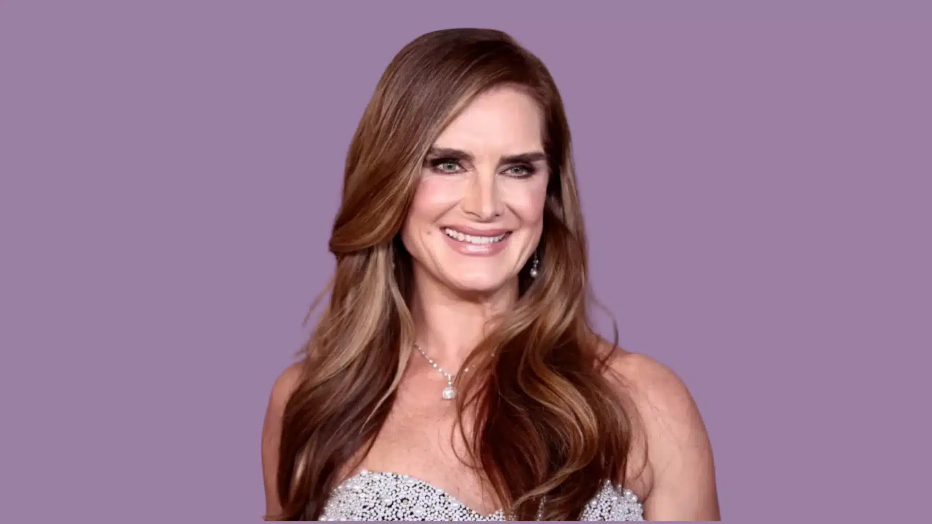 An image of Brooke Shields' height, she is smiling in a strapless, embellished gown with long brown hair against a solid lavender background