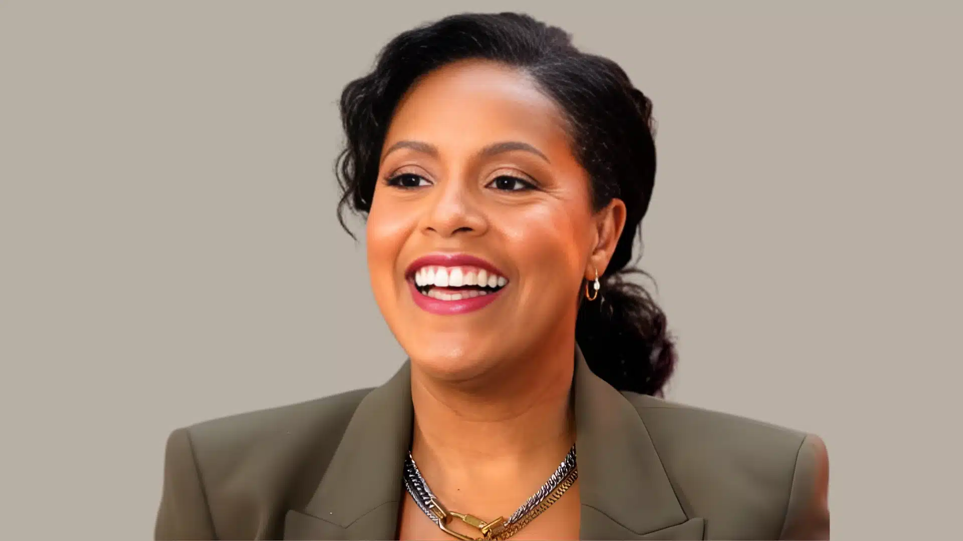An image of Sheinelle Jones' Today show host, wearing a khaki blazer and a gold and silver chain necklace against a neutral background