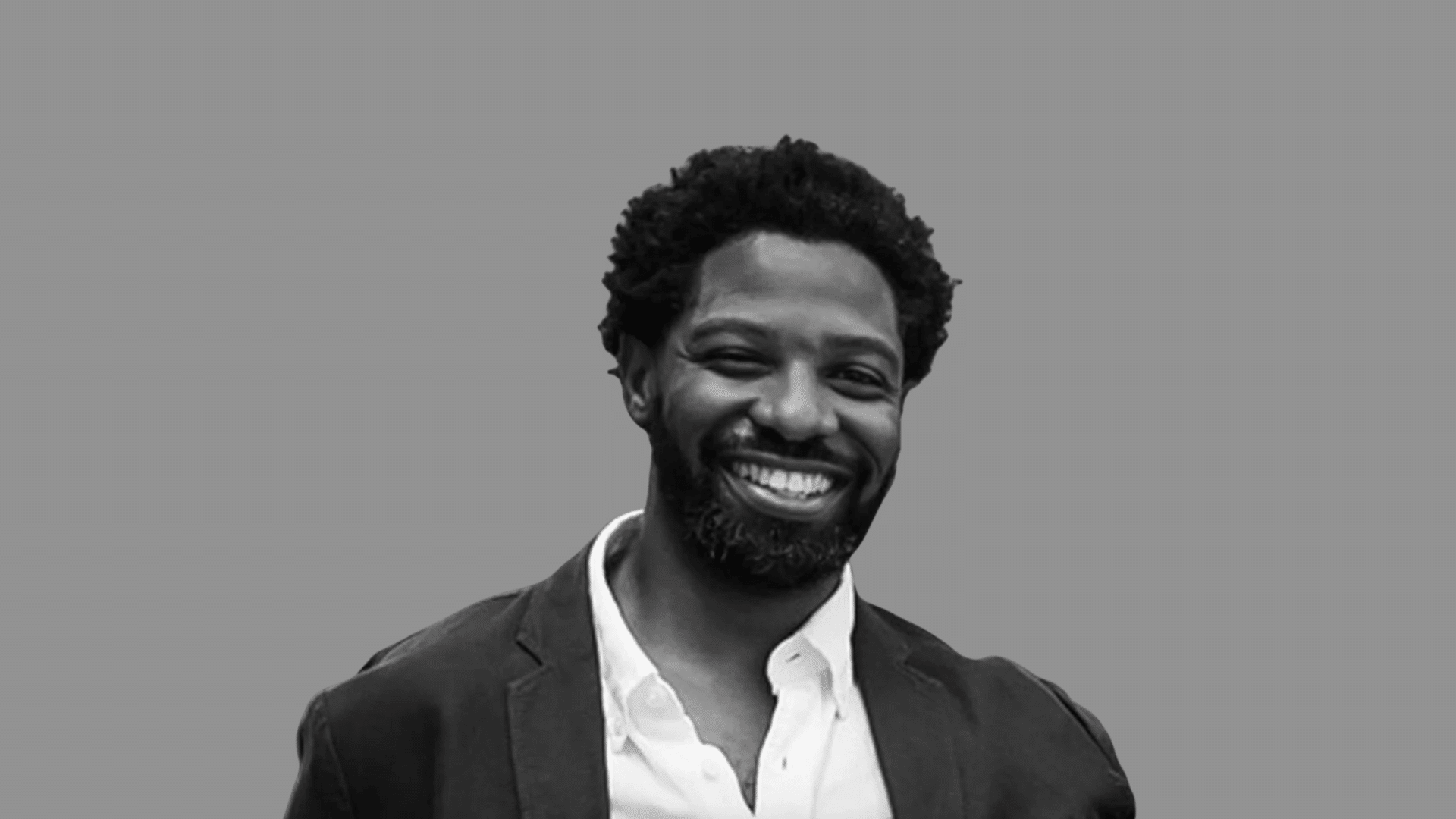An image of Uche Ojeh, husband of Sheinelle Jones, smiling, with a beard, wearing a suit jacket and a white shirt against a gray background