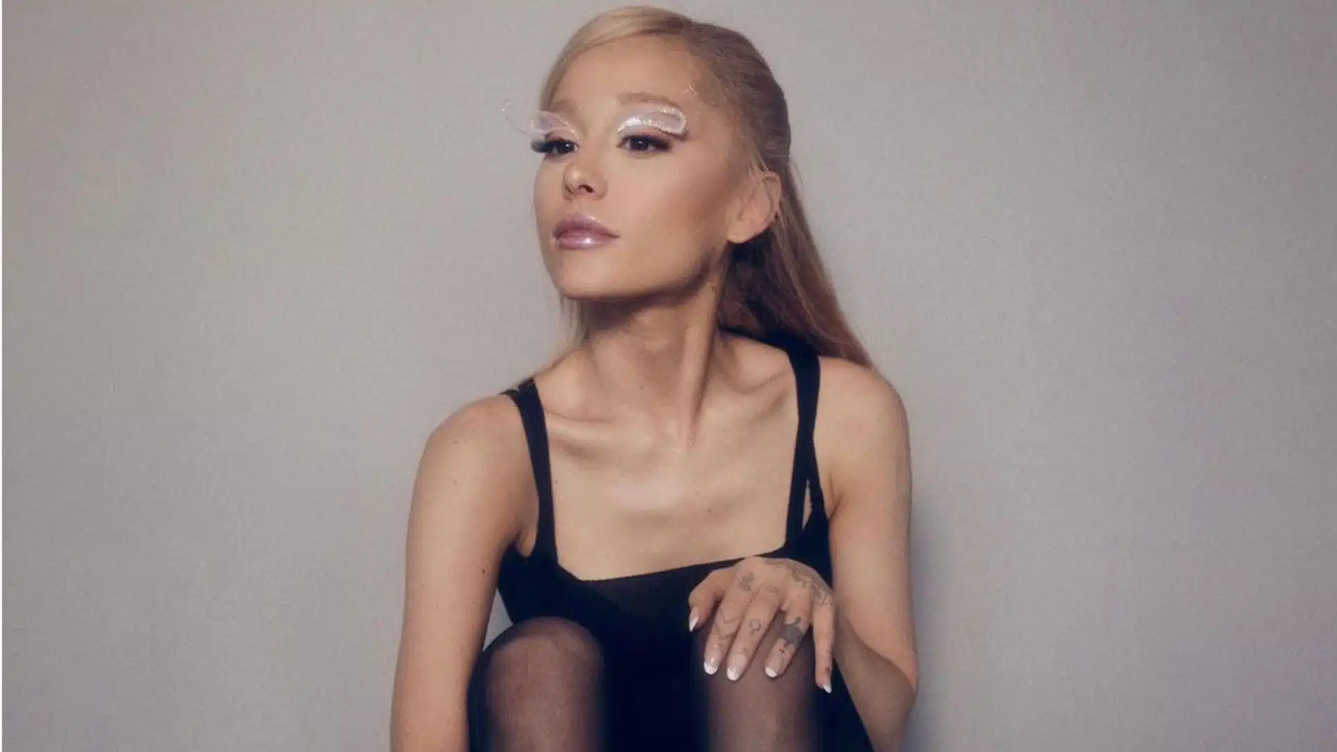 Ariana Grande's weight loss, she’s sitting in a black tank top with glittery white eye makeup against a plain gray background