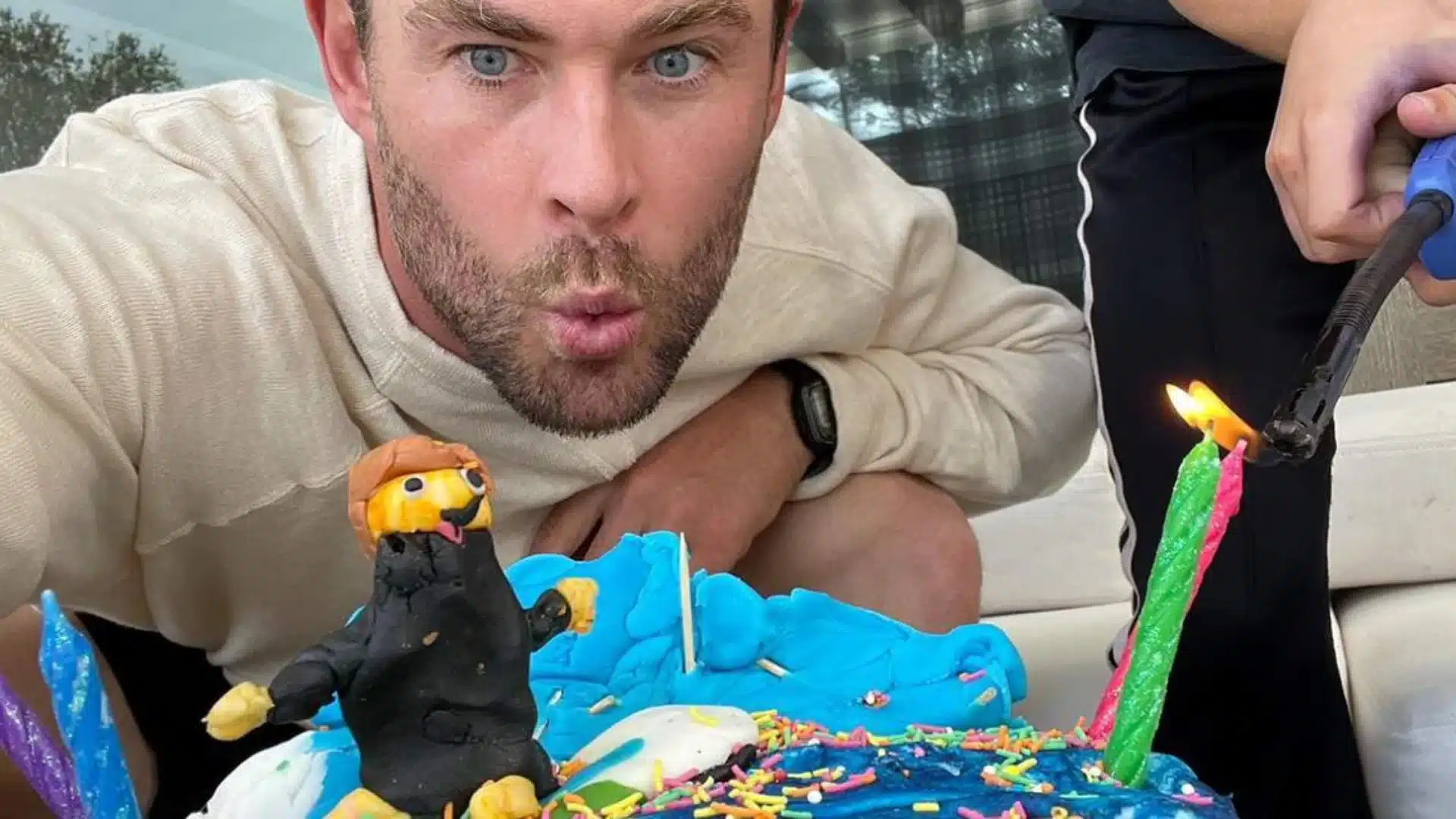 Chris Hemsworth with a homemade cake decorated with blue frosting, sprinkles, and a clay figure on his borthday