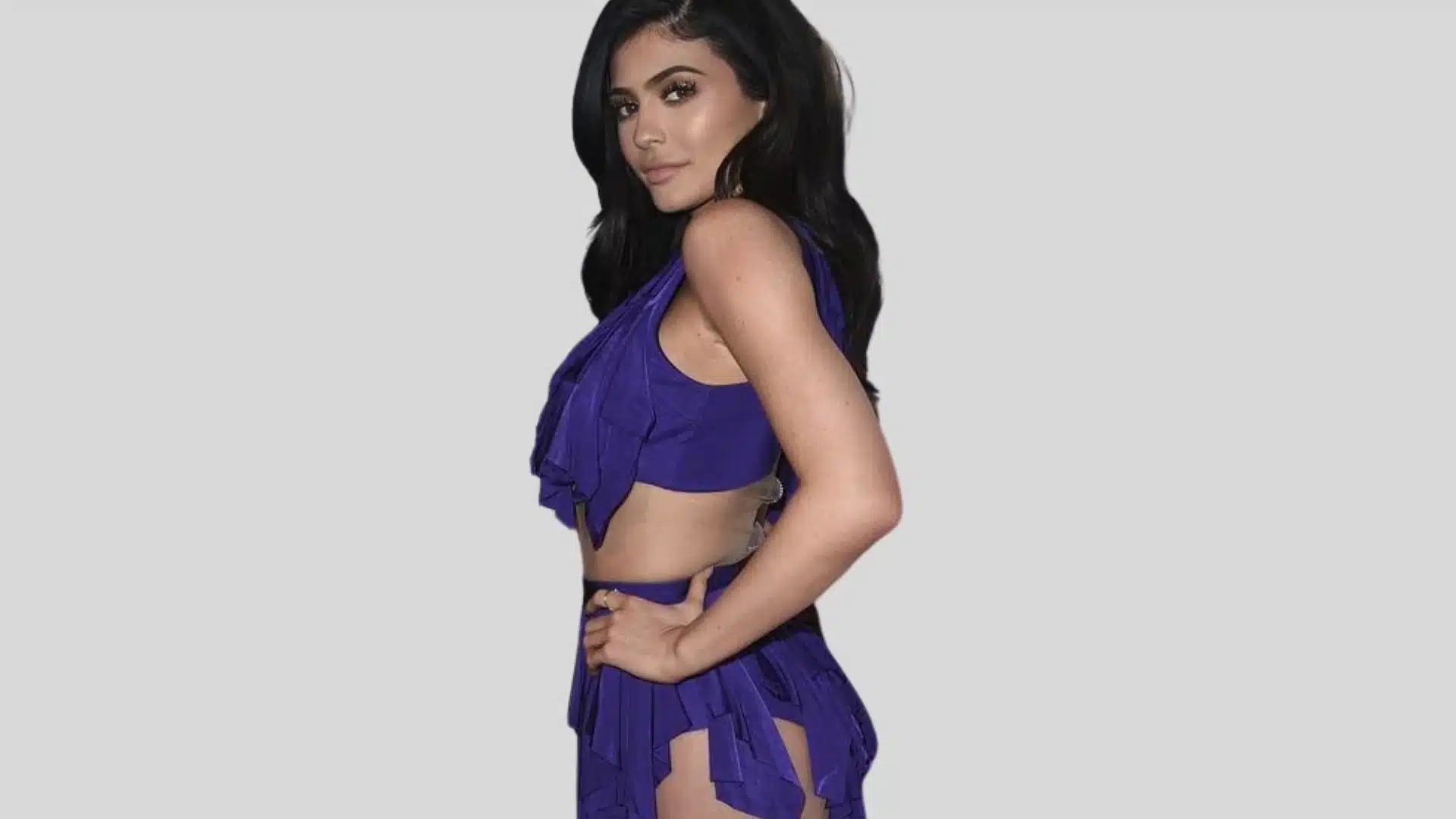 Kylie Jenner is wearing a ruffled, bright purple two piece outfit with a soft makeup look