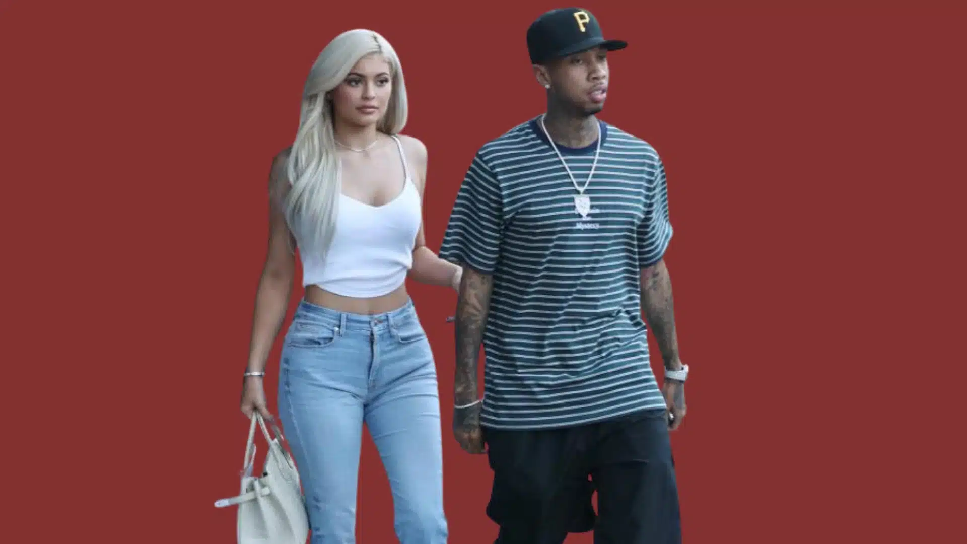 Kylie Jenner with blonde hair and bold makeup look with Tyga, standing together against a solid reddish-brown background