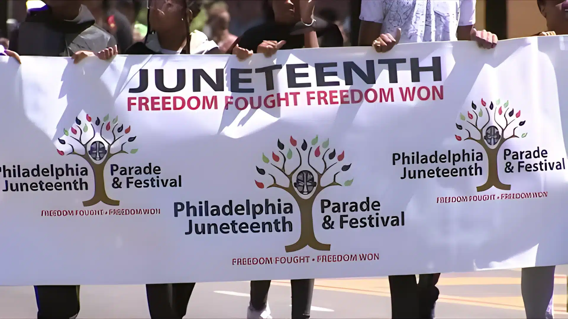 Participants holding a large banner advertising the Philadelphia Juneteenth Parade & Festival with the slogan Freedom Fought Freedom Won
