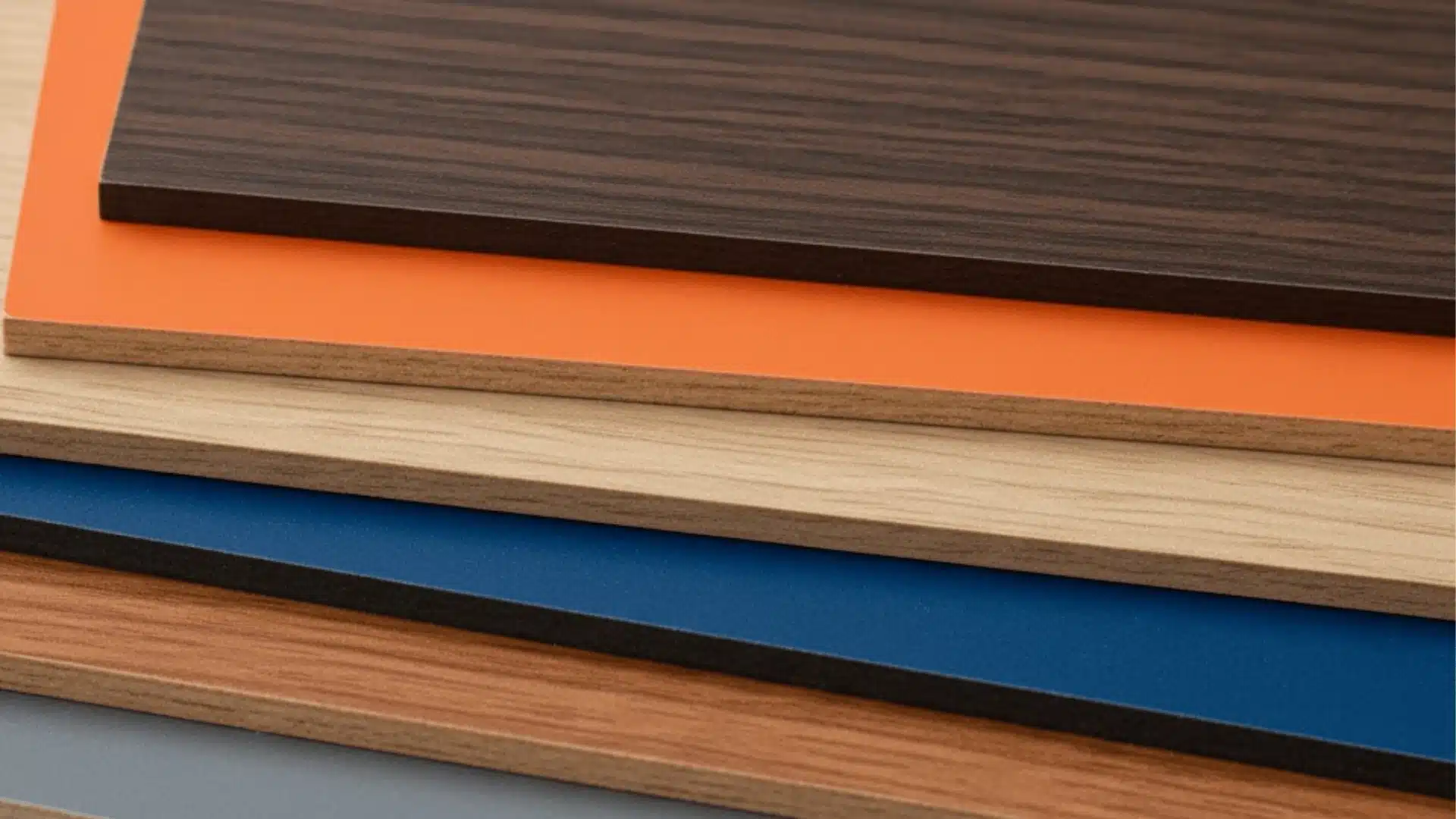 Stack of overlapping medium-density fiberboard veneer and solid color composite material samples in brown, orange, light wood, and blue