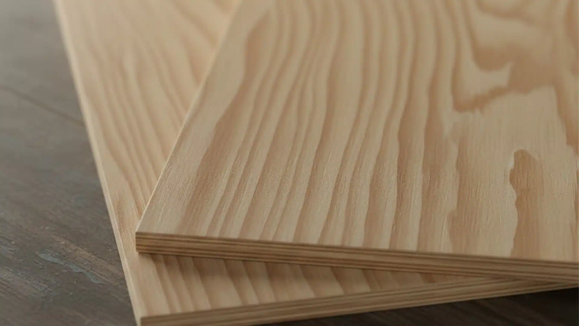 Two stacked sheets of light-brown color plywood with visible grain and layered edges rest on a dark wooden surface