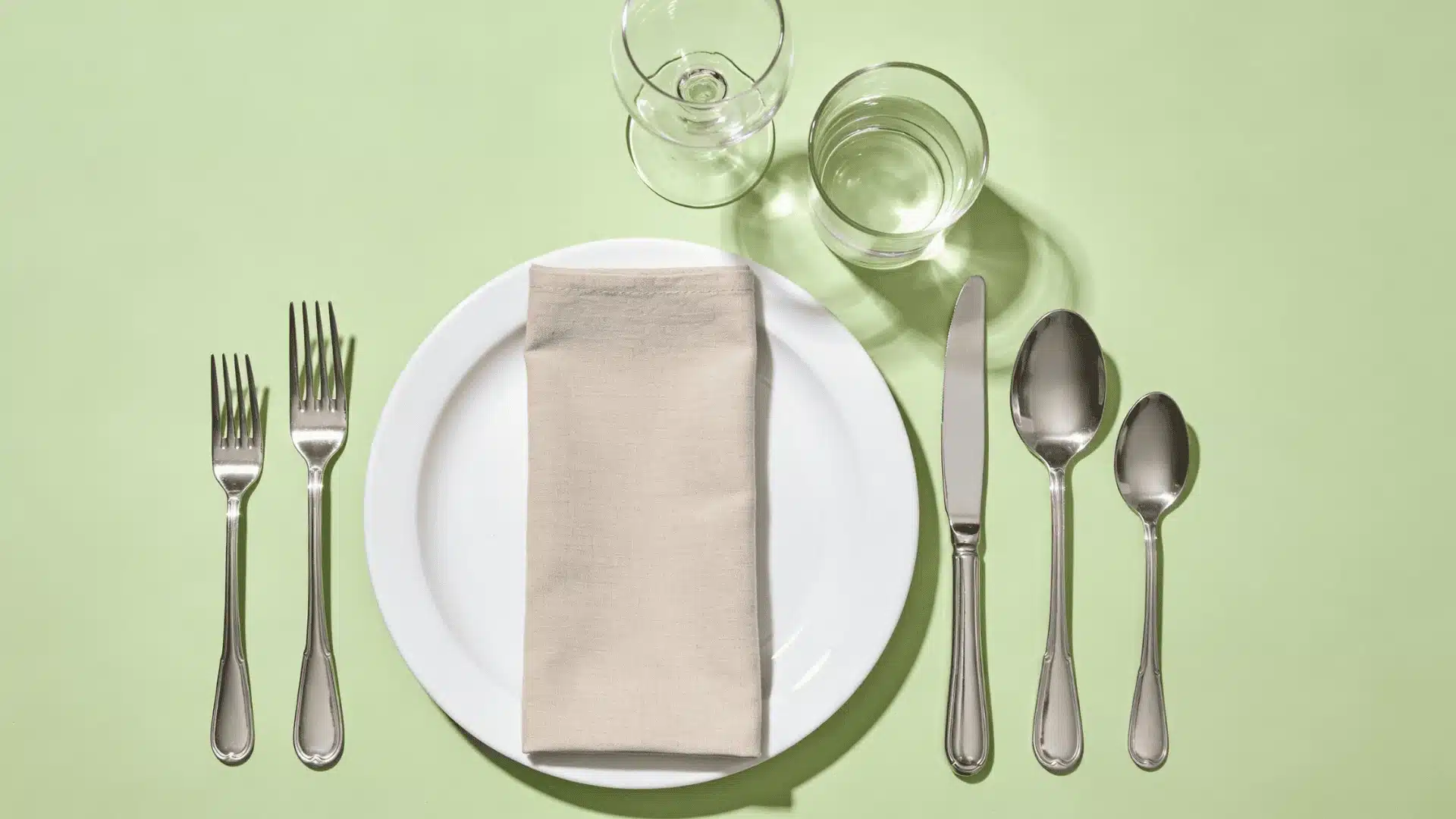 Informal table setting diagram featuring a white plate with silverware glass and a neatly folded napkin on top