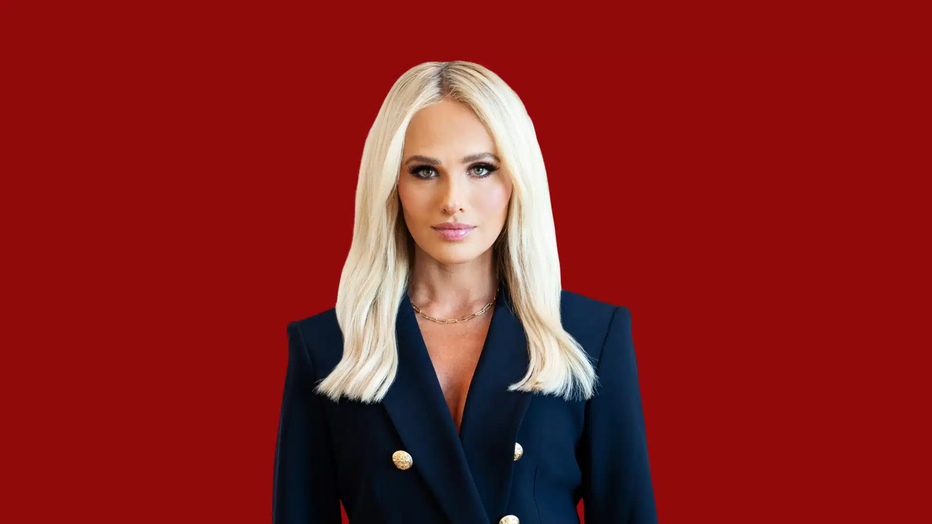 Tomi Lauren's net worth is in the talks, she is wearing a navy double breasted blazer with gold buttons against a deep red background