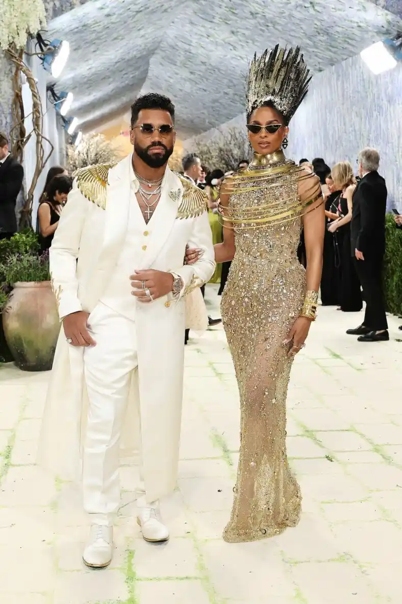 Russell wears a gold winged cream suit while Ciara stands in a sequin gown with gold hair paint