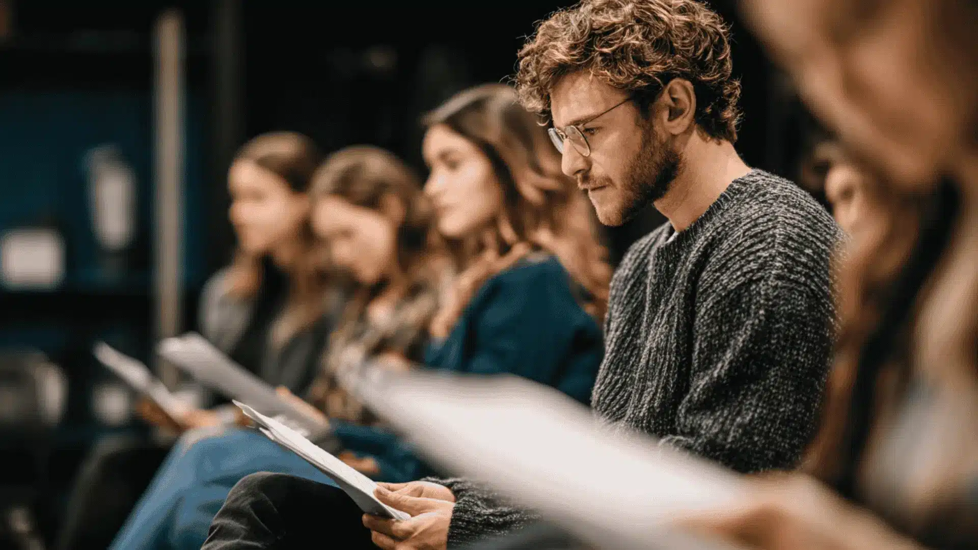 A group of people sitting in a row focused on reading scripts practicing techniques for quick memorization