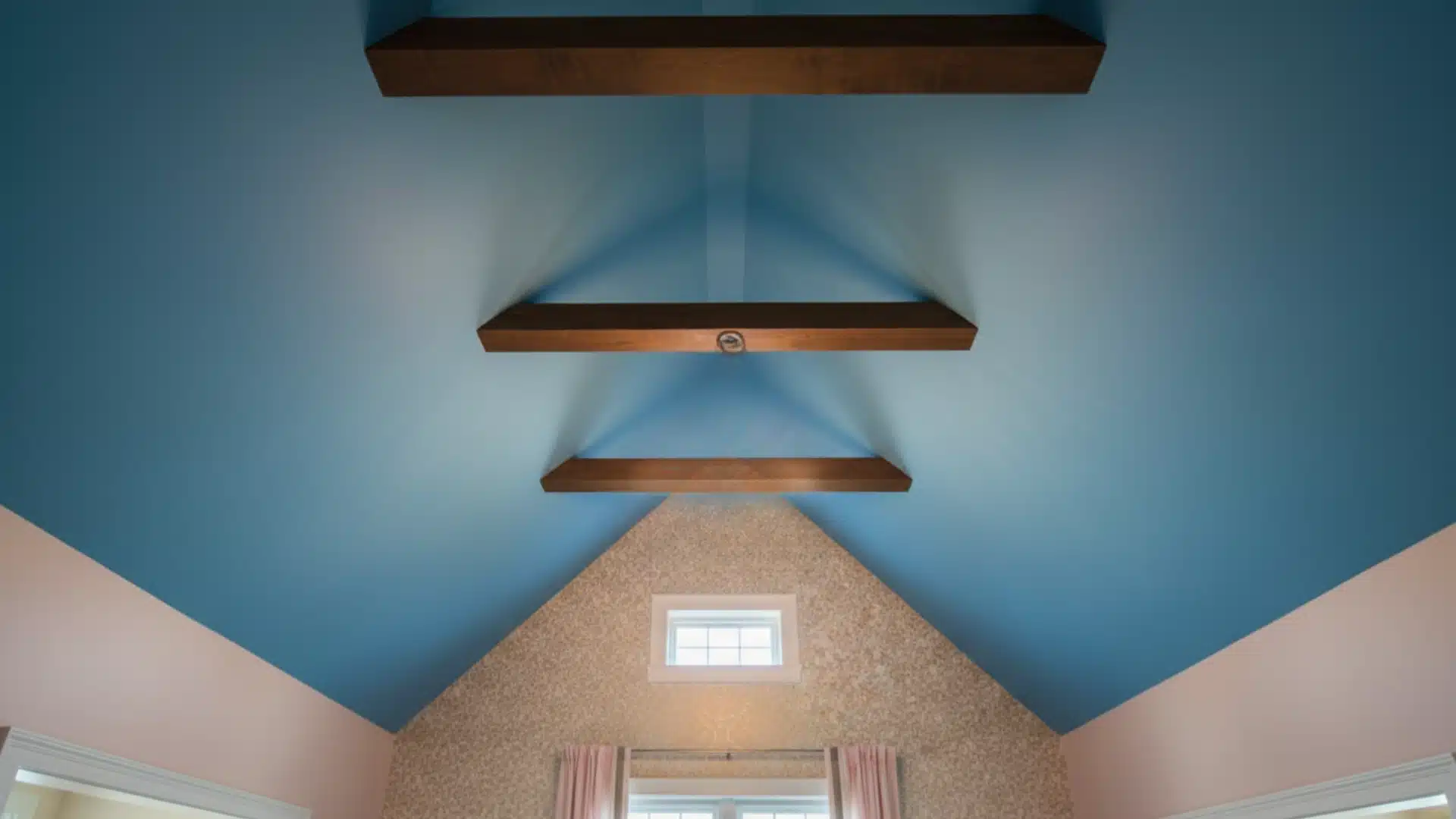 Cathederal interior ceiling painted bright blue with three prominent dark wooden beams, contrasting with light pink and textured tan walls below.