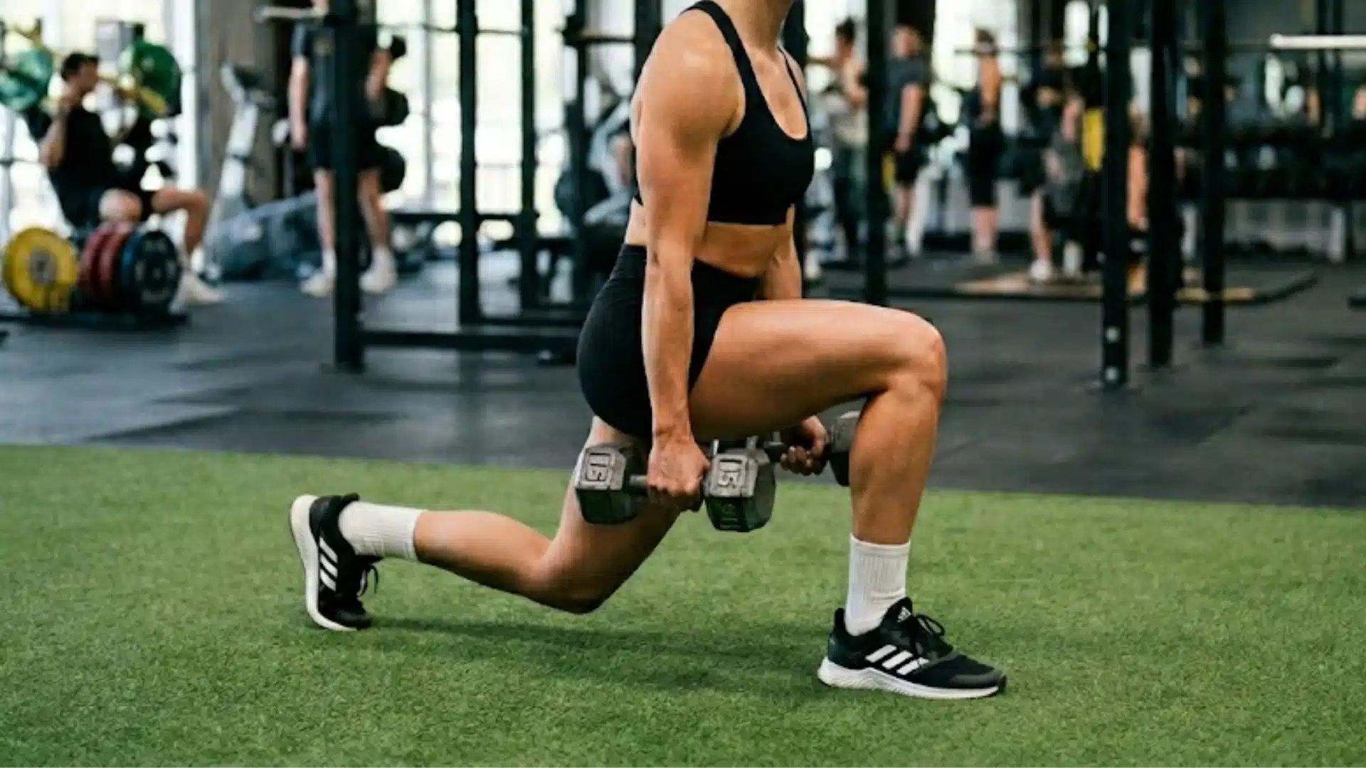 Person performing a dumbbell lunge in a gym, focusing on lower body strength with weights on indoor training floor